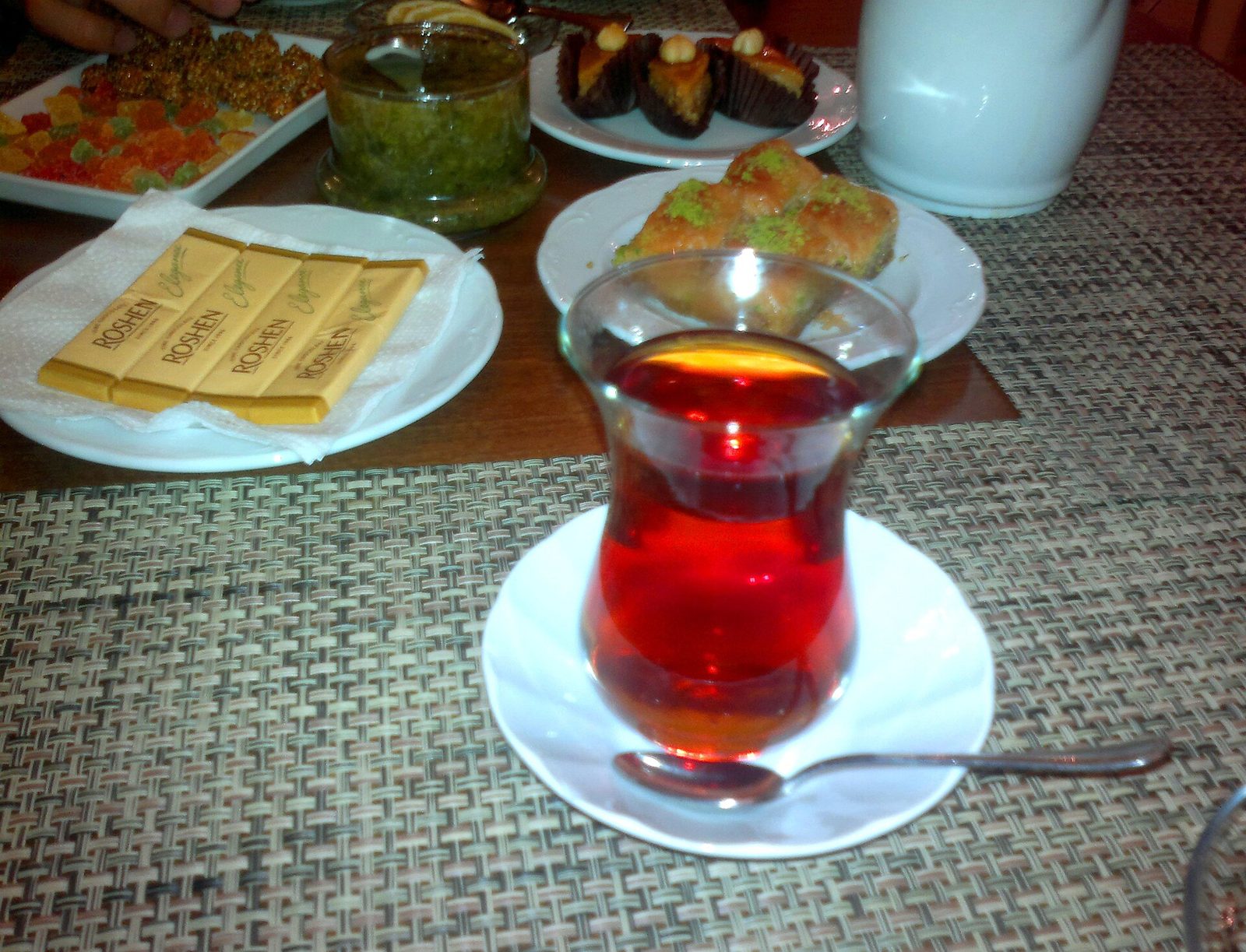Red-amber tea in a pear-shaped armudu glass on a white saucer, with sweets behind
