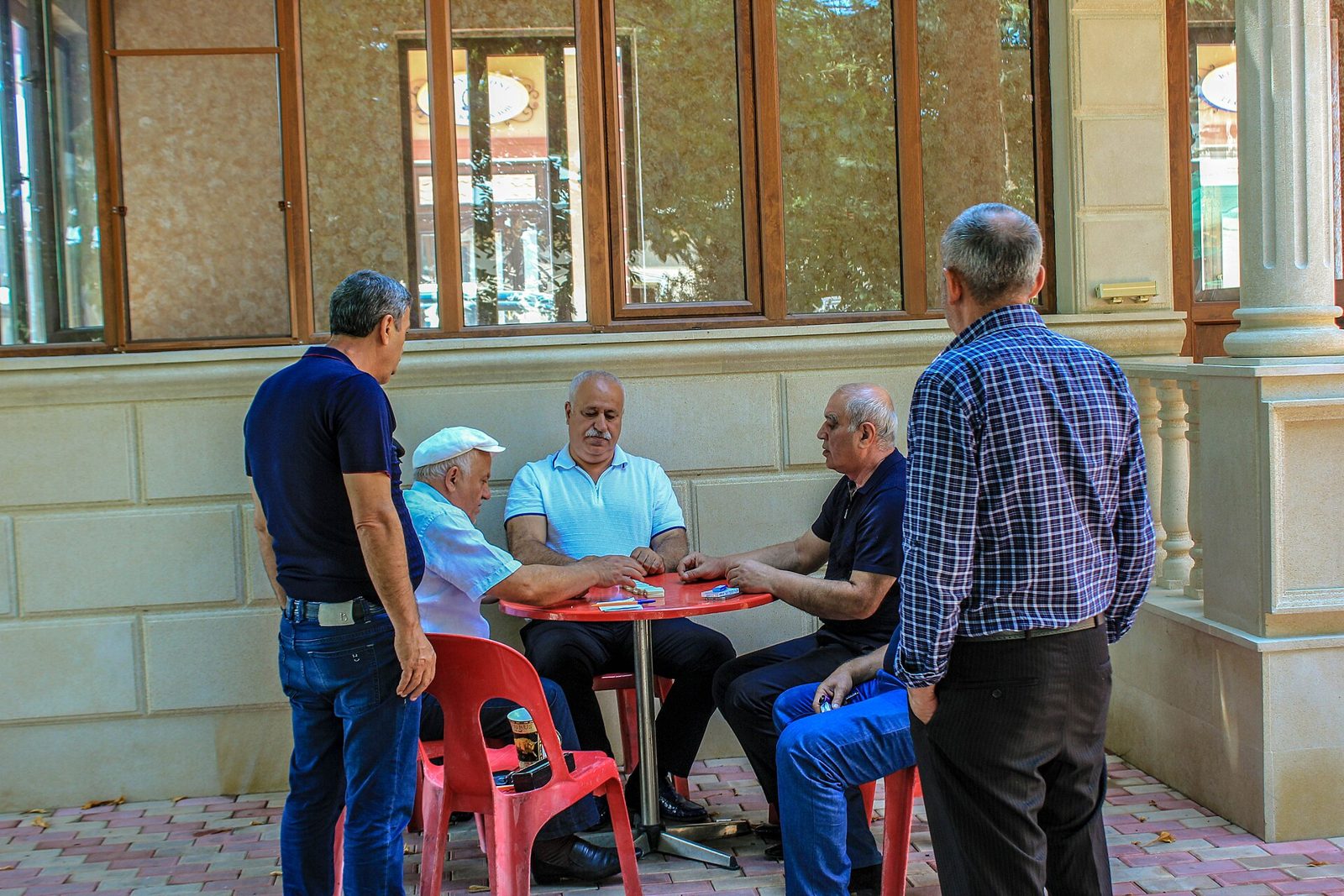 A group of men gathered around a small table outside a chaykhana, playing a game