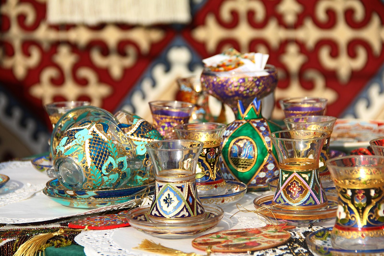 Gilded and hand-painted armudu tea glasses with matching saucers on a patterned cloth