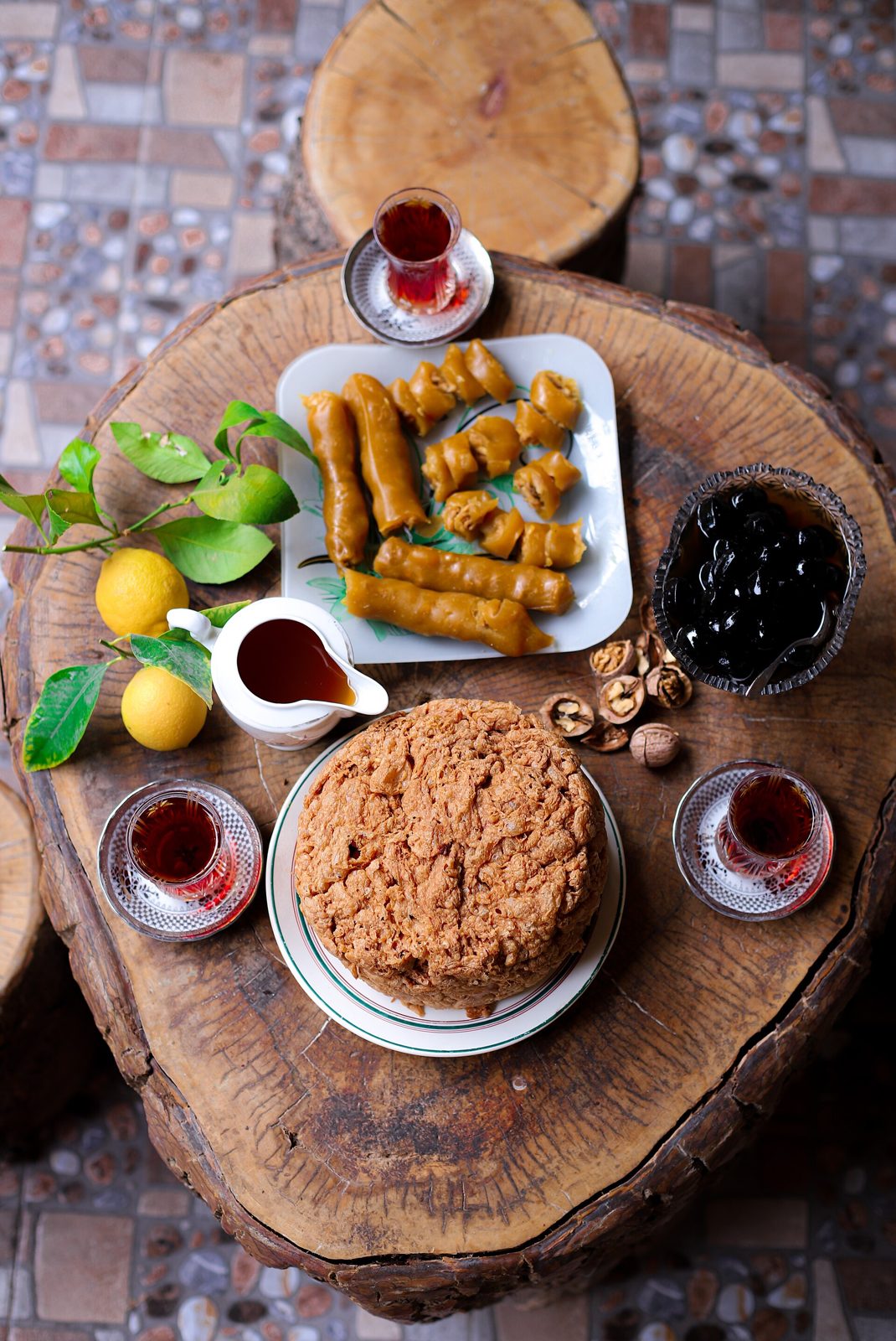 Overhead view of a wooden board with glasses of tea, pastries, jam and lemons