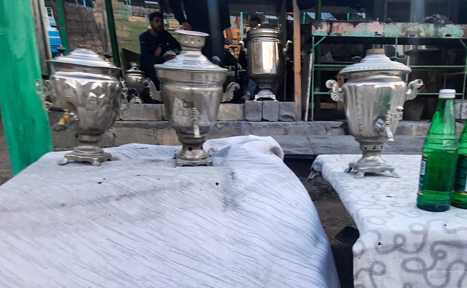 Three polished samovars on tables covered with white cloths in the village of Laza