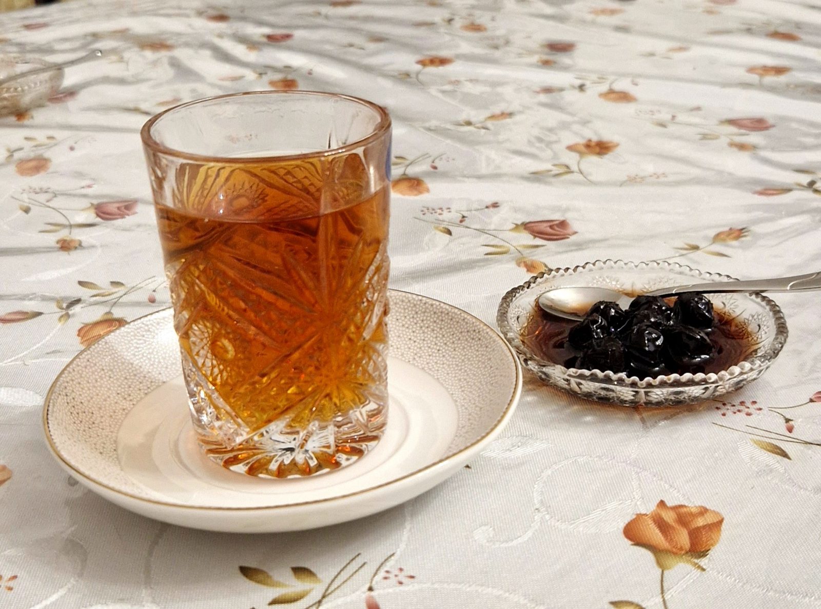 A glass of Azerbaijani black tea on a saucer next to a small dish of cherry jam