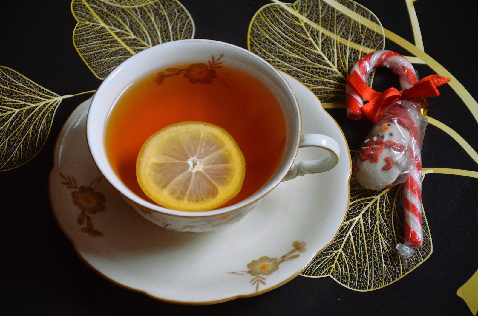 A china cup of tea with a slice of lemon and a candy cane on a dark table