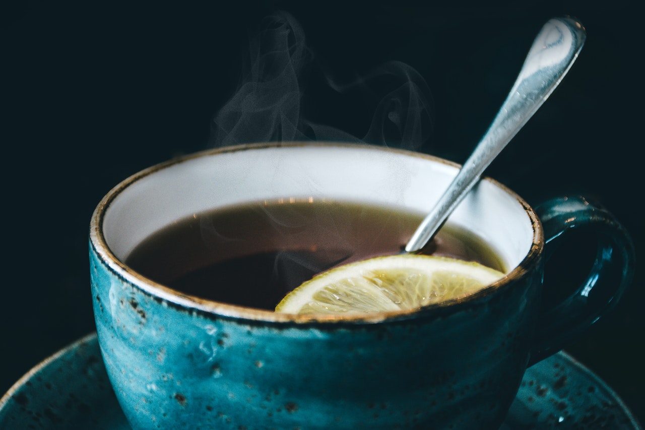 A steaming cup of black tea with a slice of lemon and a spoon