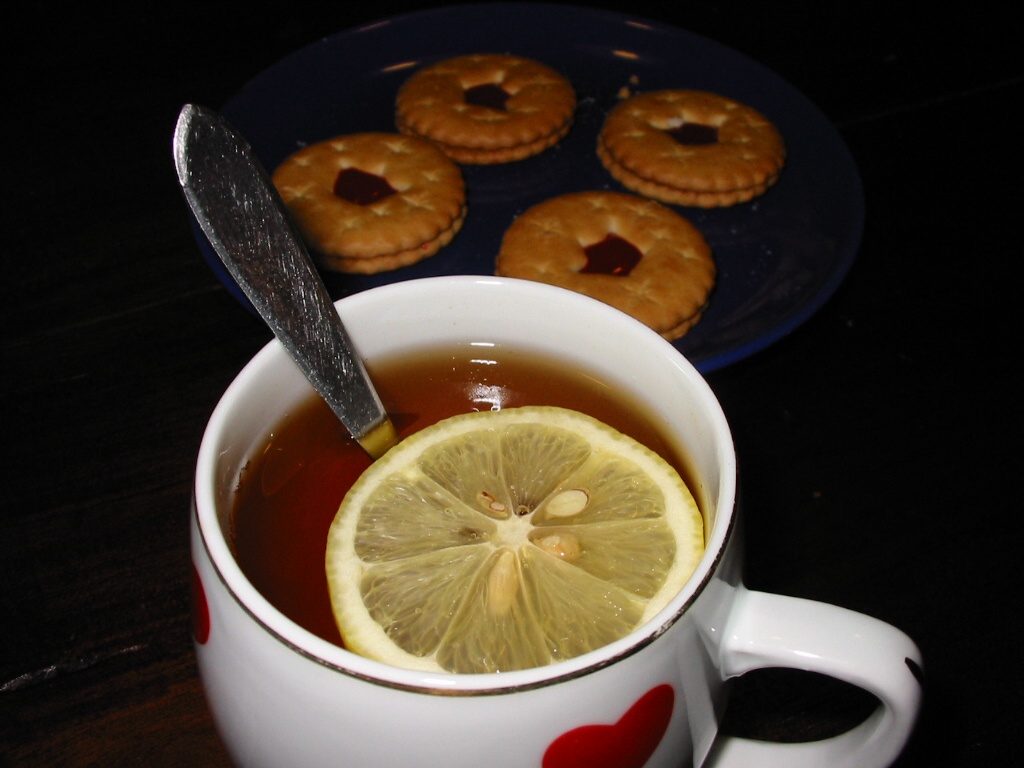 A cup of black tea with lemon next to a plate of jam biscuits