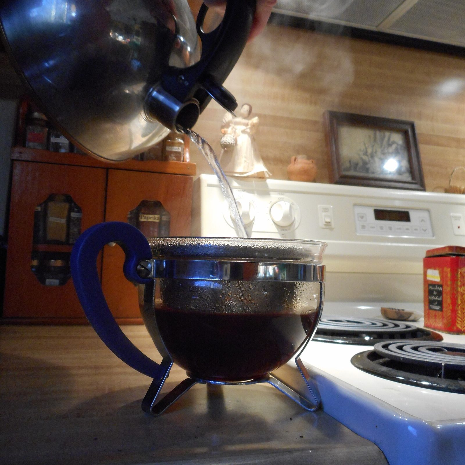 Boiling water being poured from a kettle into a glass teapot with loose tea