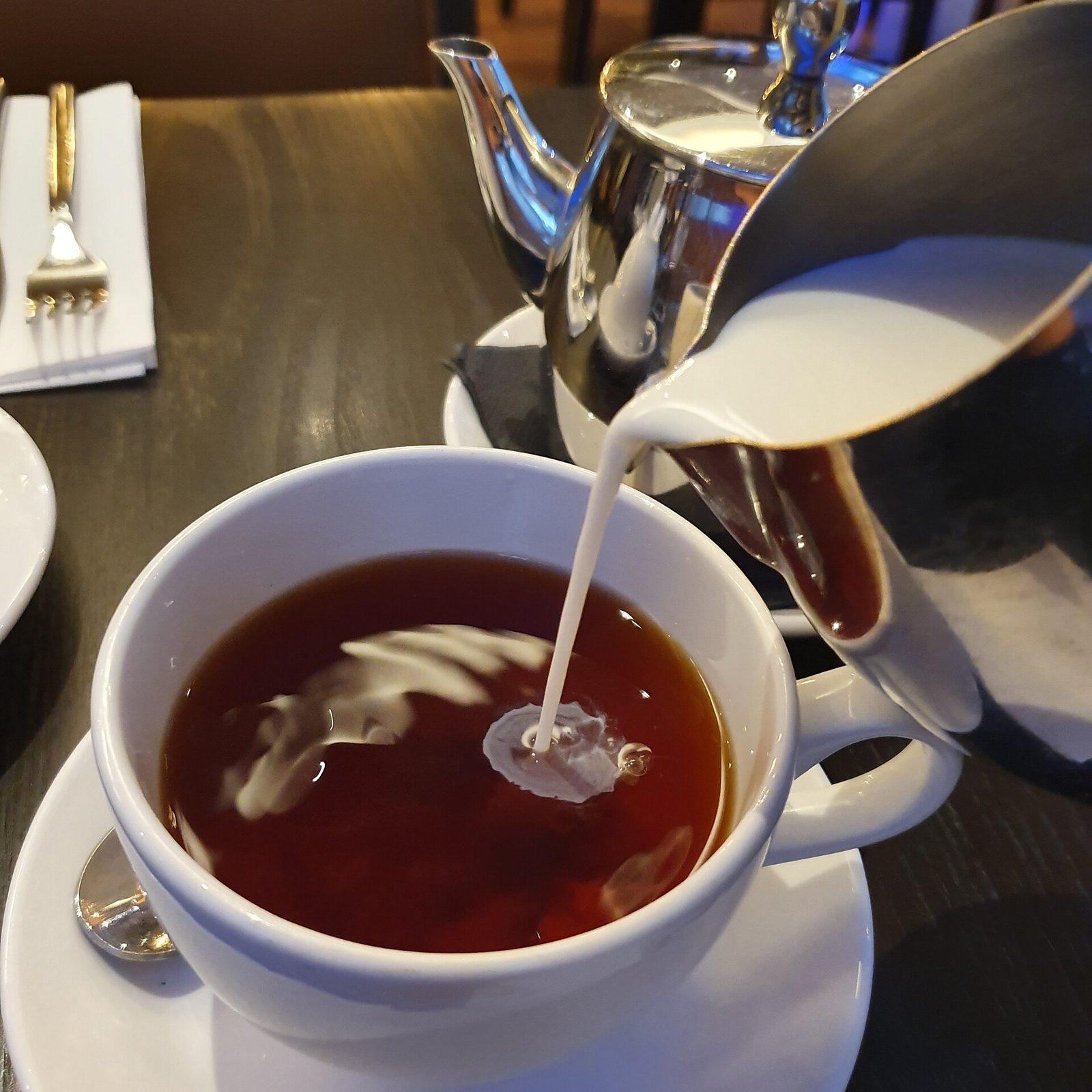 Milk being poured from a small jug into a cup of black tea