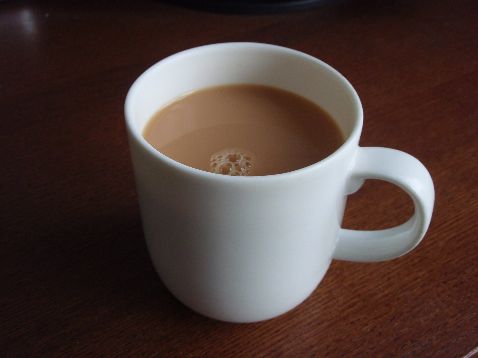 A white mug of British black tea with milk on a wooden table