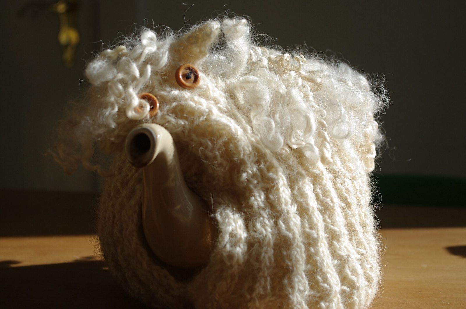 A teapot wearing a knitted woolly sheep tea cosy
